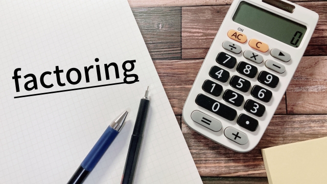 濃い茶色の木製テーブルに白い紙と電卓、二本の鉛筆が置かれている様子