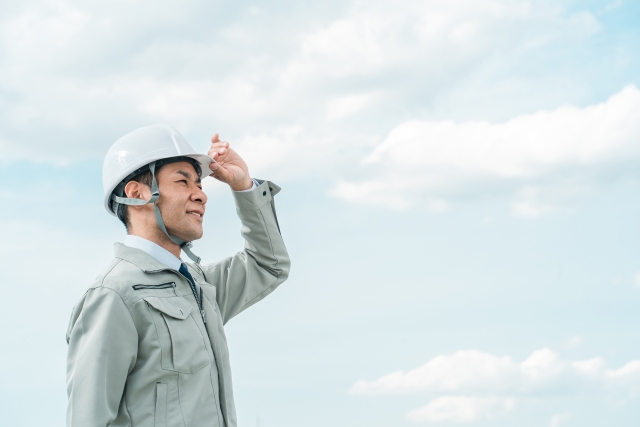 作業員がヘルメットのつばを上げ、青空を爽やかに見上げている様子
